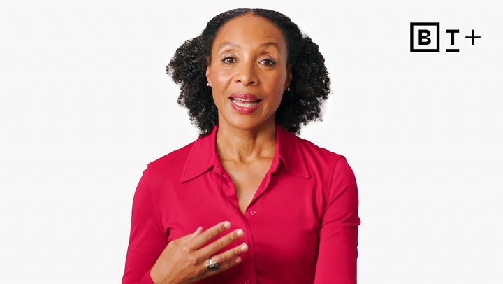 A woman in a red shirt speaks, gesturing with her right hand against a plain white background with a stylized "BT+" logo in the upper right corner.