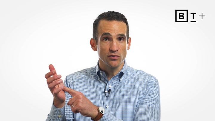 A man in a button-up shirt gestures with his hands while speaking, with a "B T +" logo in the top right corner against a white background.