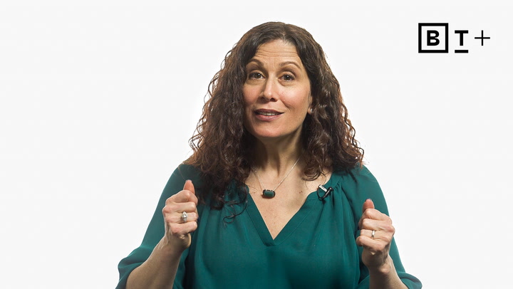 A woman with curly brown hair in a teal blouse gestures with both hands against a plain white background with a "B T+" logo in the top right corner.