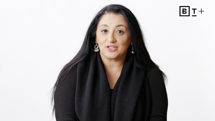 Woman with long black hair wearing a black top and earrings sits against a plain white background; BT+ logo in the top right corner.
