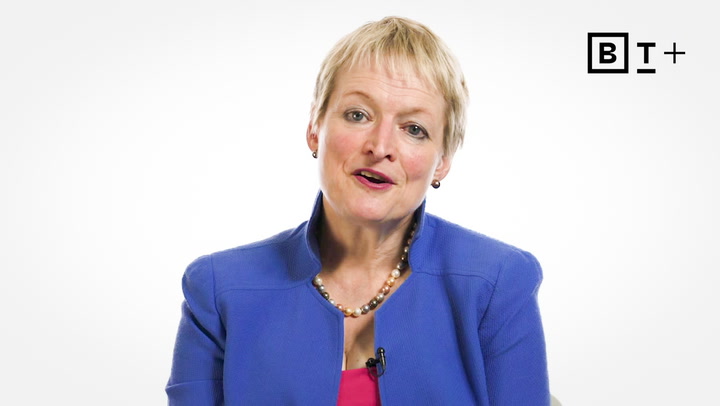 A woman with short blonde hair wearing a blue blazer and pearl necklace speaks in front of a white background with a "BT+" logo in the top right corner.