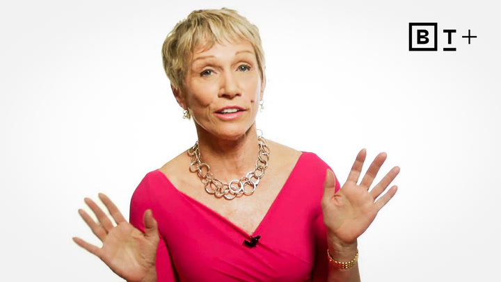 A woman in a pink dress and silver necklace gestures with both hands, facing the camera. A "BT+" logo appears in the top right corner on a white background.