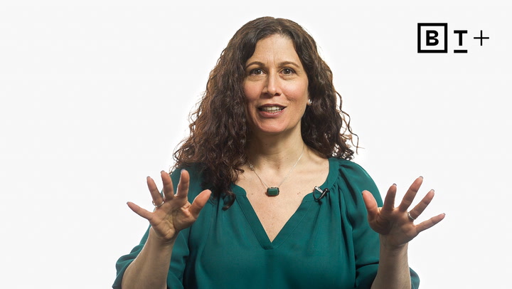 A woman with long curly hair wearing a green blouse gestures with both hands while speaking in front of a white background with a BT+ logo.