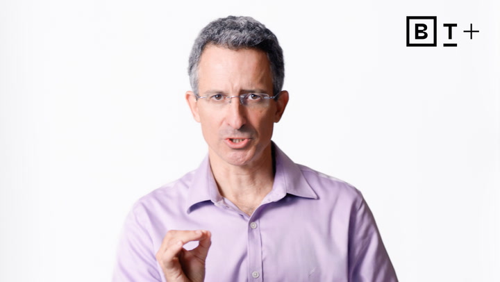 A man in a light purple shirt and glasses speaks while gesturing with his hand. A "BT+" logo appears in the top right corner on a plain white background.