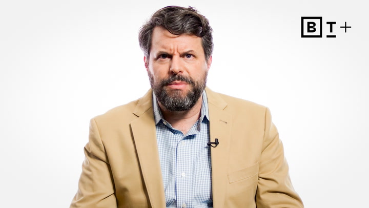 A man with a beard and mustache wearing a tan blazer and blue checkered shirt sits in front of a white background with a “B T+” logo in the top right corner.