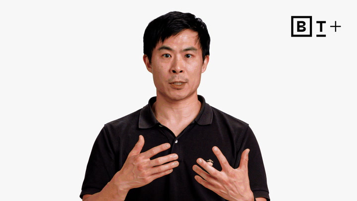 A man in a black polo shirt gestures with his hands while speaking, against a plain white background with a "B T +" logo in the top right corner.
