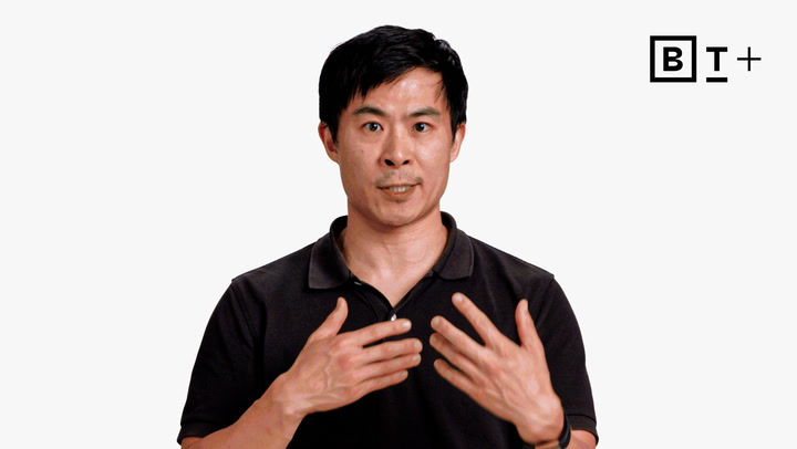 A man in a black polo shirt gestures with both hands on his chest, standing in front of a white background with a "B T +" logo in the top right corner.