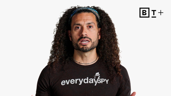 Man with long curly hair and a headband wears a black "everydayspy" shirt, speaking in front of a plain white background with a "B T +" logo in the corner.