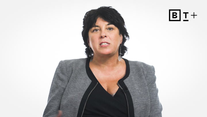 A woman with dark hair wearing a gray blazer and black top speaks in front of a plain white background with a "BT+" logo in the top right corner.