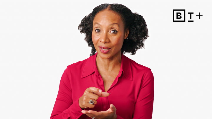 A woman in a red blouse gestures with her hands while speaking. A "B T +" logo is visible in the top right corner against a plain white background.