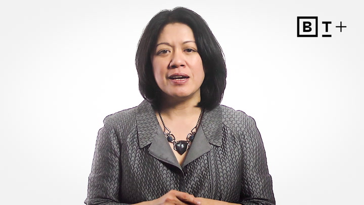 A woman in a gray textured jacket stands against a white background with a "BT+" logo in the upper right corner.