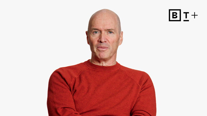 A middle-aged man in a red sweater sits against a plain white background with a "B T +" logo in the top right corner.