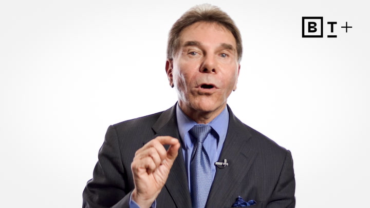 A man in a suit and tie speaks while gesturing with his hand; a "BT+" logo appears in the top right corner against a white background.