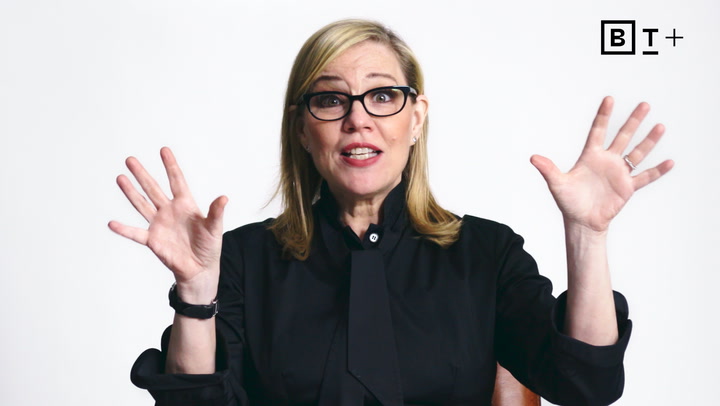 A woman with glasses and blonde hair in a black outfit speaks with hands raised, in front of a plain white background with a "BT+" logo in the corner.
