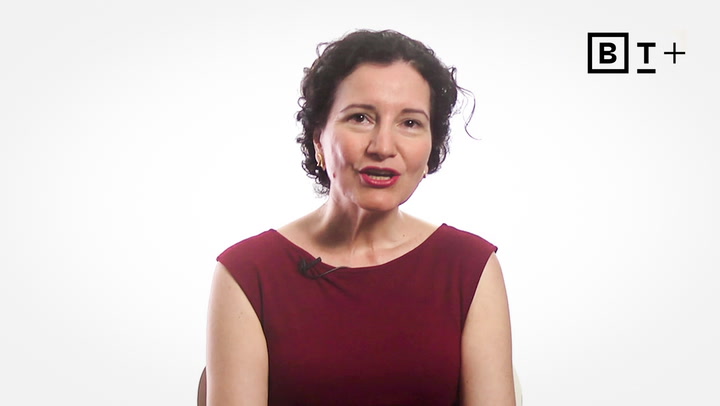 A woman with short curly dark hair wearing a sleeveless maroon top sits against a white background with a BT+ logo in the top right corner.