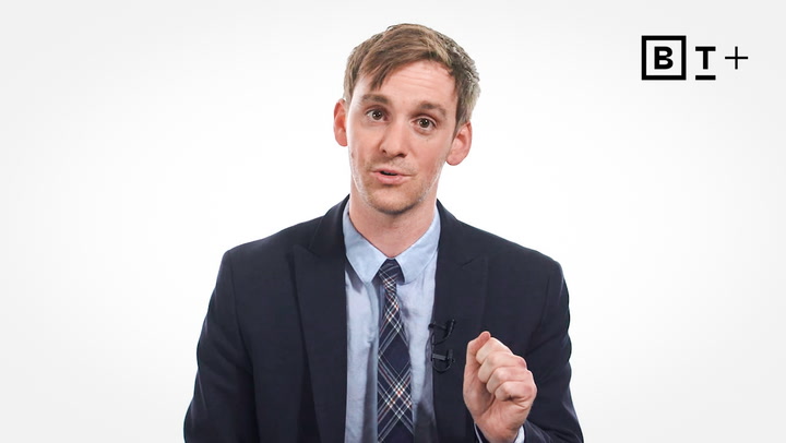 A man in a suit and tie gestures while speaking in front of a white background with a black "BT+" logo in the top right corner.