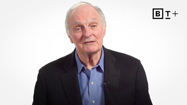 An older man with gray hair wearing a dark blazer and blue shirt speaks in front of a plain white background with a "B T+" logo in the upper right corner.