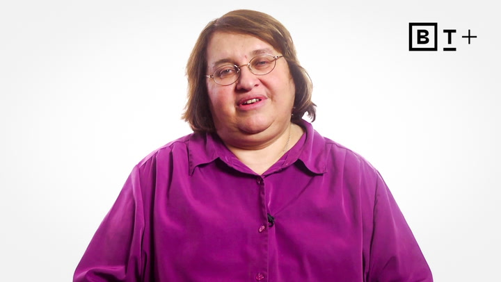 A person with short brown hair wearing glasses and a purple shirt stands in front of a plain white background with a "B T +" logo in the top right corner.