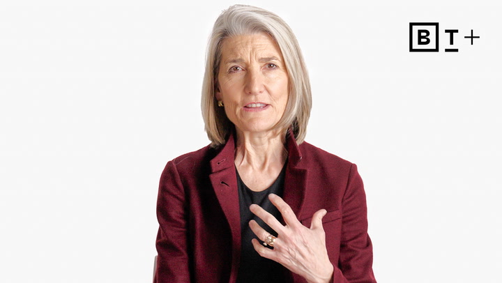 A woman with gray hair in a burgundy blazer gestures with her left hand. The background is white with the "BT+" logo in the top right corner.