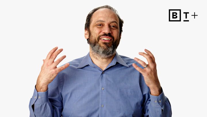 A man with a beard and mustache in a blue shirt gestures with both hands while smiling, with a "B T +" logo in the top right corner.