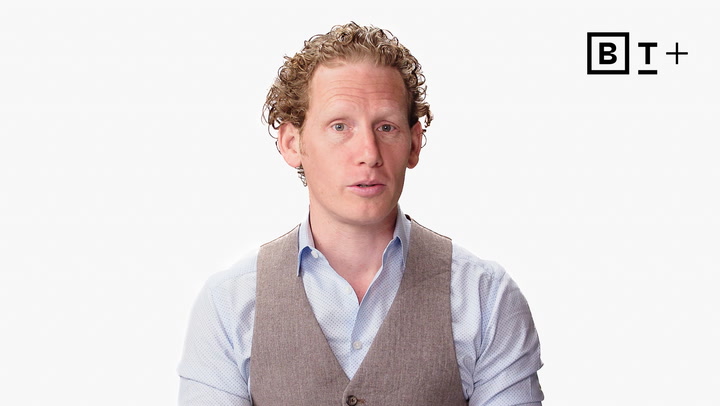 A man with curly hair wearing a light blue shirt and gray vest sits against a white background with the BT+ logo in the top right corner.