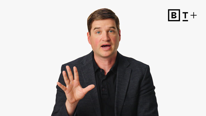 A man in a dark blazer holds up his hand while speaking, with a "BT+" logo in the top right corner against a white background.