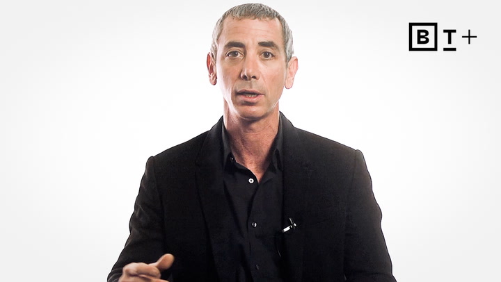A man with short gray hair, wearing a black suit and shirt, sits against a plain white background with a "BT+" logo in the top right corner.
