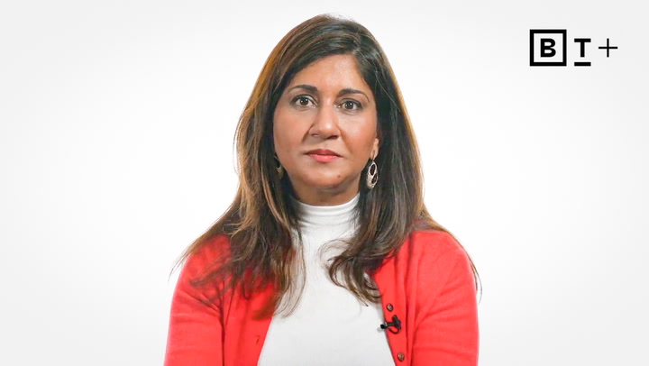 A woman with long brown hair wearing a white turtleneck and red cardigan sits against a white background with a "BT+" logo in the top right corner.