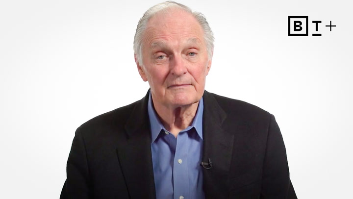 An older man with gray hair wearing a blue shirt and dark blazer sits against a plain white background with a "BT+" logo in the top right corner.