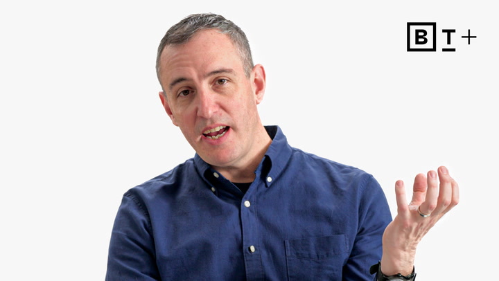 A man in a blue button-up shirt gestures with his left hand while speaking. A black and white "B T +" logo appears in the top right corner.