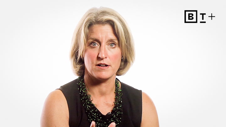 A woman with short blonde hair, wearing a sleeveless black top and a beaded necklace, speaks in front of a plain white background with a "B T +" logo in the corner.