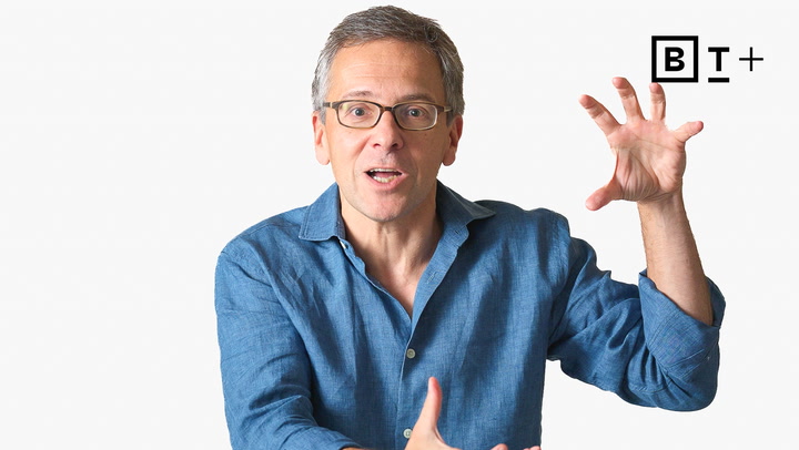 A man in a blue shirt gestures with his hands while speaking in front of a white background with a "B T +" logo in the top right corner.