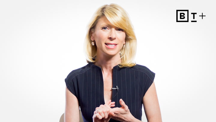 A woman with blonde hair wearing a navy pinstripe top speaks while gesturing with her hands, seated against a white background with a "BT+" logo in the corner.