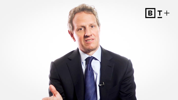 A man in a dark suit and blue tie sits facing the camera against a plain white background with a "BT+" logo in the top right corner.