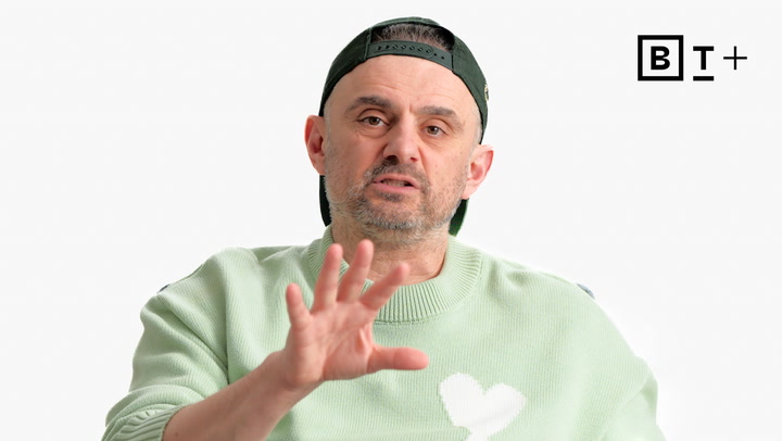 A man in a pastel green sweater and backwards cap gestures with his hand, with a "B T +" logo in the top right corner on a plain white background.