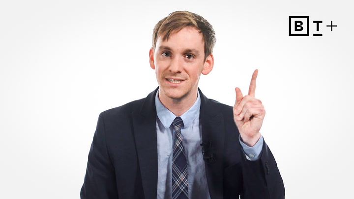 A man in a suit sits against a white background, raising his right index finger. The "B T +" logo appears in the top right corner.