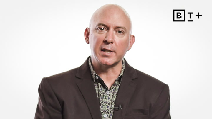 A bald man in a patterned shirt and dark blazer speaks in front of a white background with a "BT+" logo in the upper right corner.