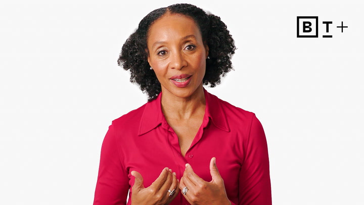 A woman with curly hair wearing a red shirt speaks while gesturing with her hands. The letters "BT+" appear in the top right corner on a white background.