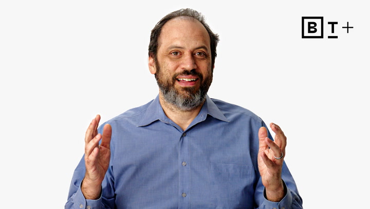 A man with a beard wearing a blue shirt gestures with both hands while speaking, with a "B T +" logo in the top right corner on a white background.
