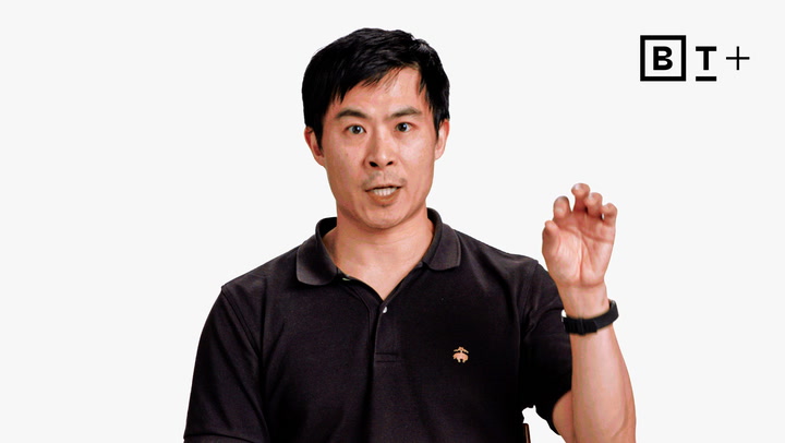 A man in a black polo shirt gestures with his hand while speaking, with a "B T +" logo in the top right corner on a plain white background.