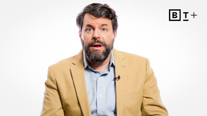 A man with a beard in a tan blazer and checked shirt sits in front of a white background with the "B T+" logo in the top right corner.