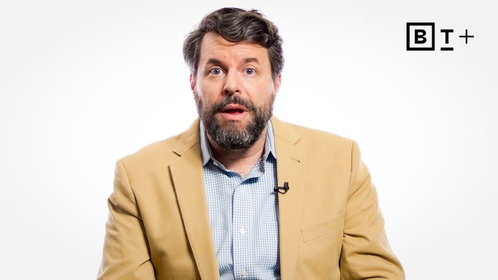 A man with a beard in a tan blazer and checked shirt sits in front of a white background with the "B T+" logo in the top right corner.