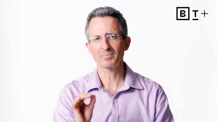 A middle-aged man in glasses and a light purple shirt gestures with his hand against a plain white background. A "BT+" logo is visible in the top right corner.