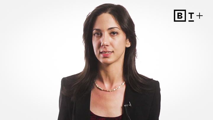 A woman with long dark hair, wearing a black blazer and necklace, sits in front of a white background with a BT+ logo in the top right corner.