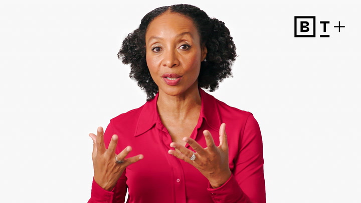 A woman in a red blouse gestures with her hands while speaking in front of a plain white background with the BT+ logo in the top right corner.