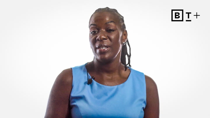 A person wearing a light blue sleeveless top and a microphone headset stands in front of a plain white background with a "BT+" logo in the top right corner.