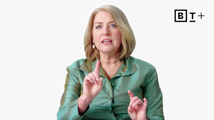 A woman with blonde hair wearing a green blouse gestures with her hands, sitting against a plain white background with a "B T +" logo in the top right corner.