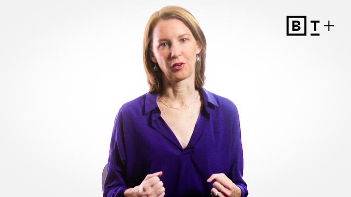A woman with shoulder-length brown hair wearing a purple blouse stands against a white background with the BT+ logo in the top right corner.
