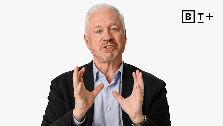 An older man with white hair and a beard, wearing a suit jacket and shirt, gestures with his hands while speaking against a plain white background with a "B T +" logo in the corner.