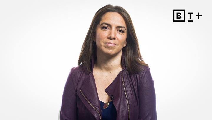 A woman with long brown hair wearing a purple jacket sits in front of a white background with a "BT+" logo in the top right corner.